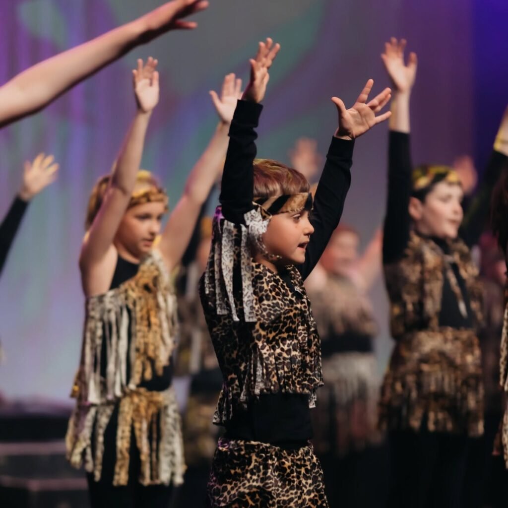 Young performers in animal-print costumes raising their arms on stage.