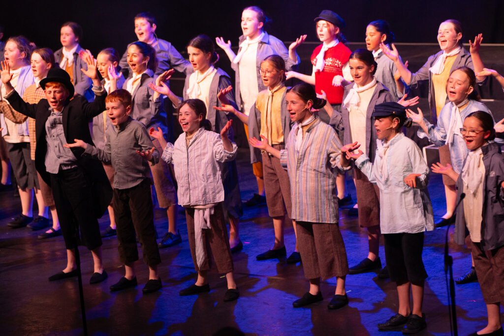 A group of young performers singing together on stage in costume.