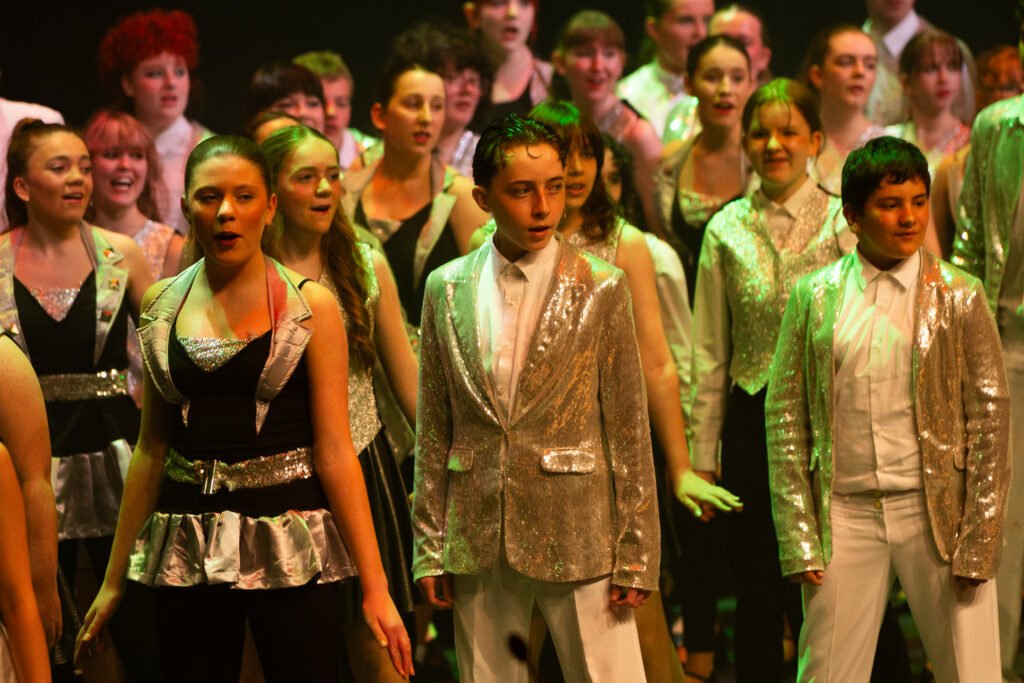 Young performers singing on stage in sparkly costumes.