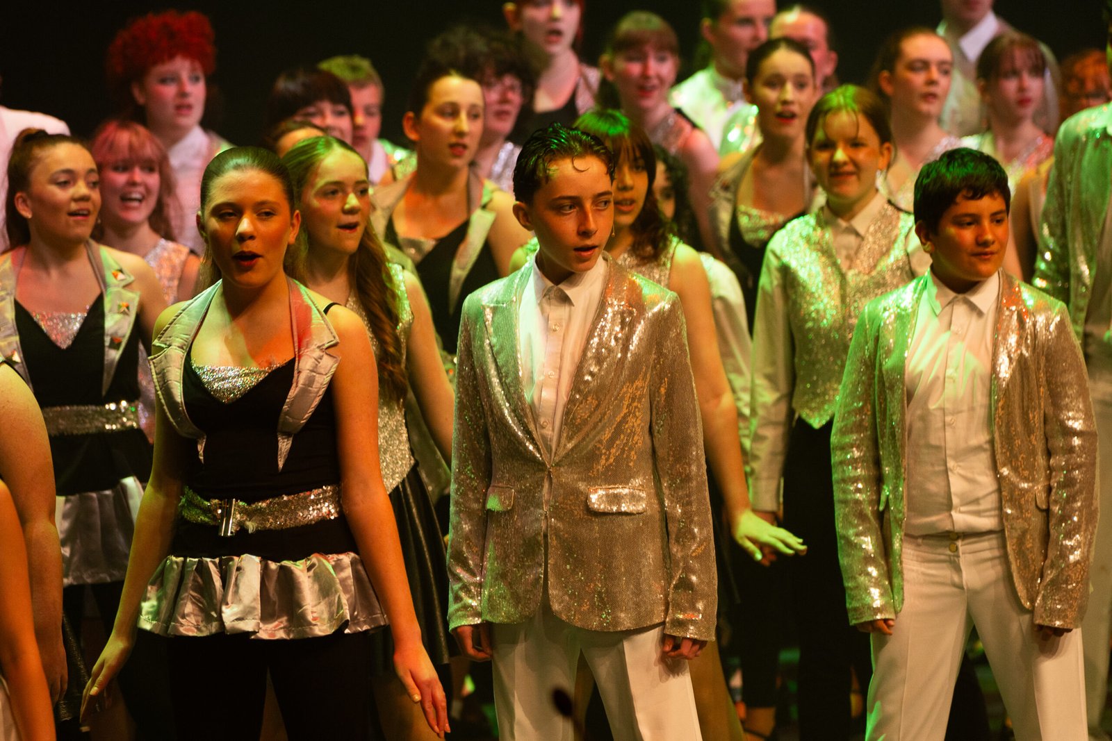 Young performers singing on stage in sparkly costumes.