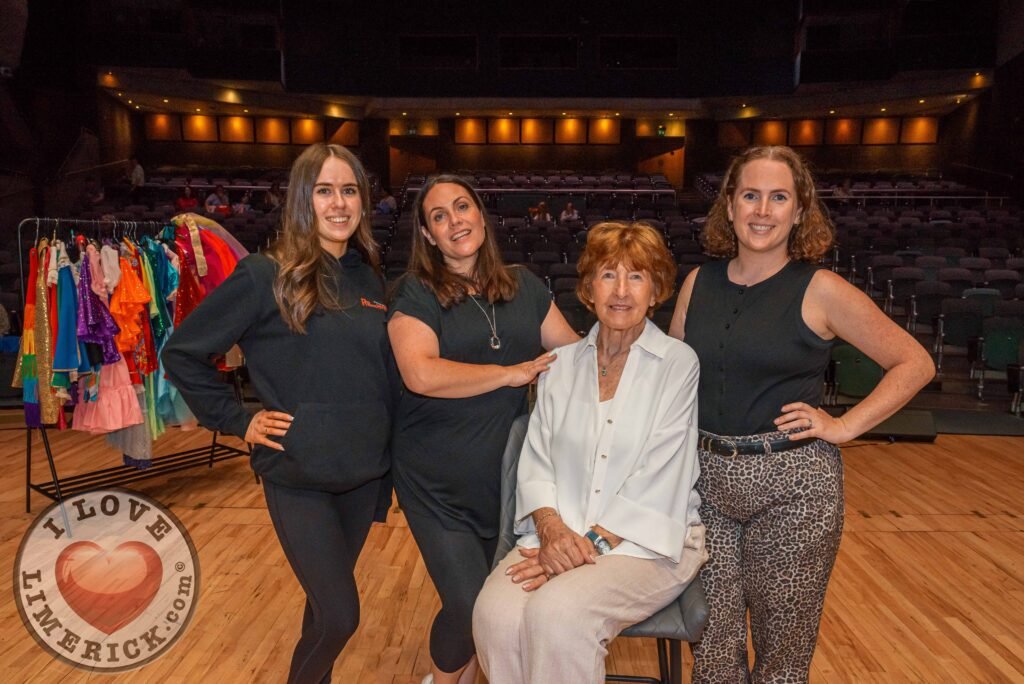 Four adults posing beside a costume rail in a theatre.