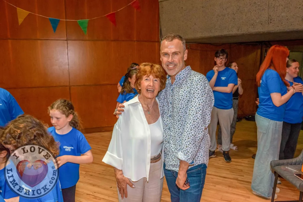 Two adults posing together with children and other adults in the background.